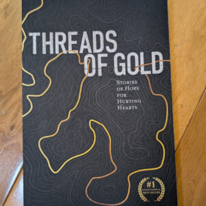 Threads of Gold book cover — black with gold contour lines, text Stories of Hope for Hurting Hearts and #1 bestseller seal.