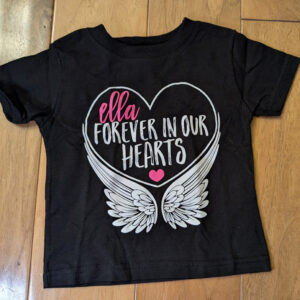 Black children's T-shirt with a heart and white angel wings, bearing the text "ella forever in our hearts" and a small pink heart.