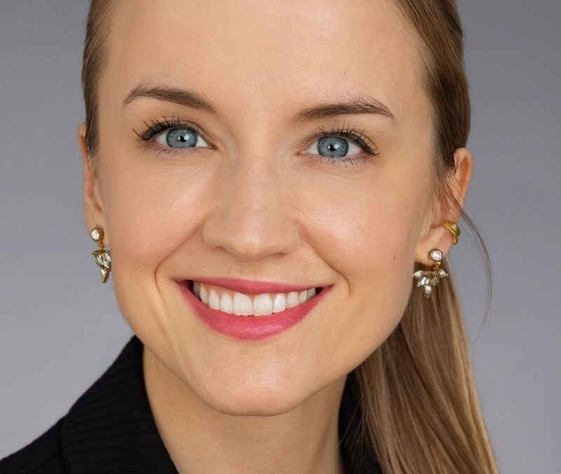 Smiling woman with blue eyes and pulled-back blonde hair, wearing pearl-and-crystal earrings and a black top